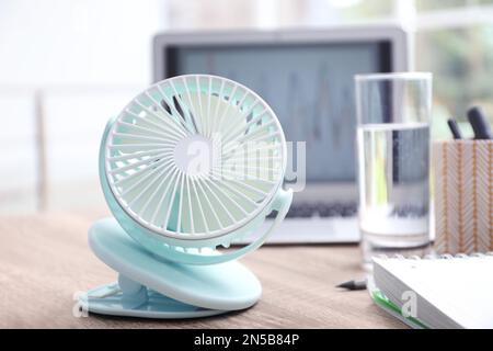 Modern portable fan on wooden table in office. Summer heat Stock Photo