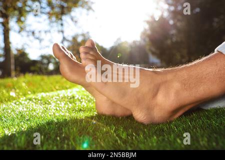 Man sitting barefoot on fresh green grass outdoors, closeup Stock Photo