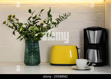 Modern yellow toaster, coffeemaker and beautiful bouquet on countertop in kitchen Stock Photo