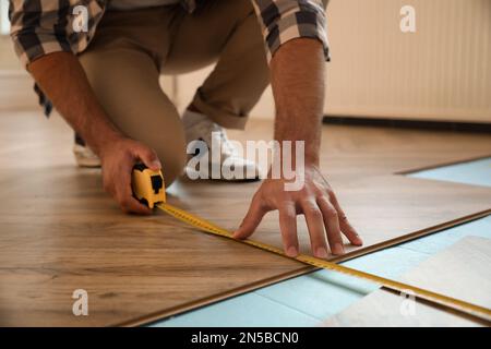 Professional worker using measuring tape during installation of parquet flooring indoors, closeup Stock Photo