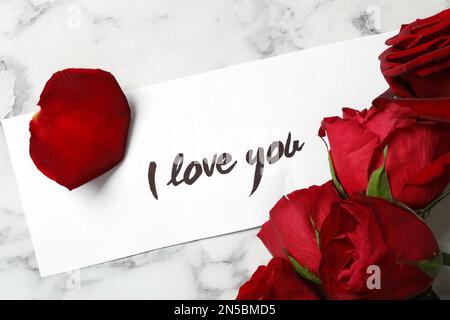 Card with text I Love You and red roses on white marble table, above view Stock Photo