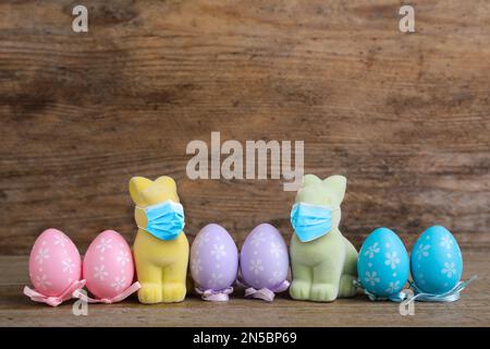 COVID-19 pandemic. Easter bunnies in protective mask and colorful eggs on wooden background Stock Photo