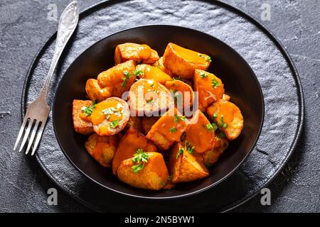 patatas bravas, deep fried potatoes with spicy sauce in black bowl on concrete table, spanish cuisine Stock Photo