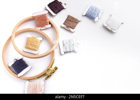 On a white background are cotton threads of different colors wound on bobbins and a round wooden hoop Stock Photo