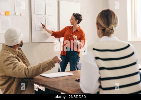 Mature businesswoman giving a presentation to her team during a meeting. Team leader discussing some reports with her colleagues. Group of creative bu Stock Photo