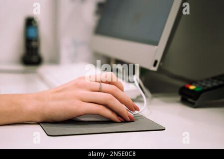 Close up hand of young woman administrator works at the reception of fitness club or health centre. Working on computer. Stock Photo