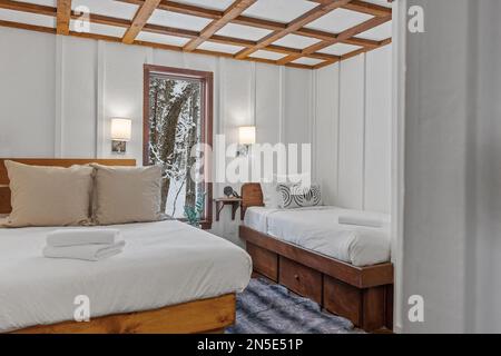 A king size bed and small bed in a white bedroom next to each other Stock Photo
