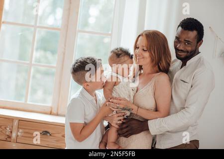 Mixed race family with white son and infant swarthy daughter spend time together at cozy apartment. African american man with his fair skinned wife ki Stock Photo