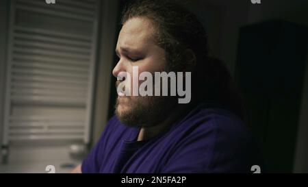 One overweight person suffering alone in front of bathroom mirror. Depression concept of a chubby man facing himself in front of mirror during hard ti Stock Photo