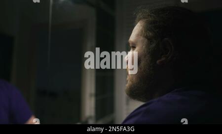 One overweight person suffering alone in front of bathroom mirror. Depression concept of a chubby man facing himself in front of mirror during hard ti Stock Photo