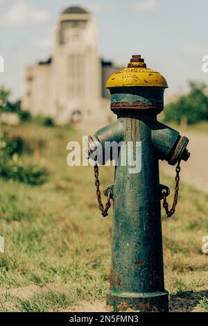 An old rusty fire hydrant on the grass in the park with a building in the blur background on a sunny day Stock Photo