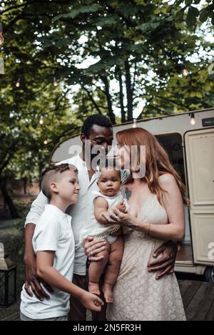 Mixed race family with white son and infant swarthy daughter spend time together in camper park outdoor. African american man with his fair skinned wi Stock Photo