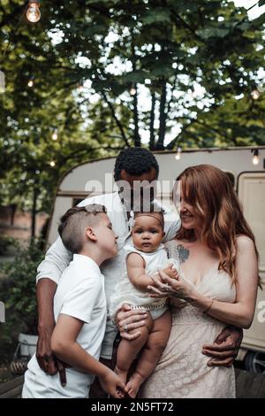 Mixed race family with white son and infant swarthy daughter spend time together in camper park outdoor. African american man with his fair skinned wi Stock Photo