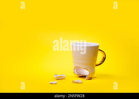 Broken tea cup isolated on yellow background. Cracked coffee mug and fragile ceramic pieces Stock Photo