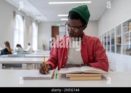 Talented young African American guy scientist wearing glasses studying in library. Education concept Stock Photo