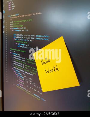 Computer screen showing python code with yellow sticker saying hello world Stock Photo