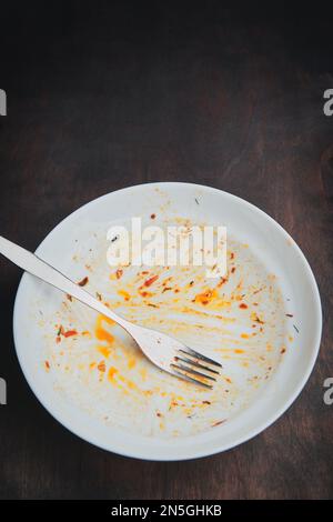 Dirty empty plate and fork. Messy dish on a wood table Stock Photo