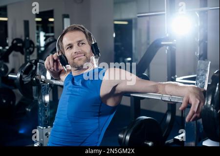 Mid adult man taking a break after exercising and listening to music in the gym, Bavaria, Germany Stock Photo