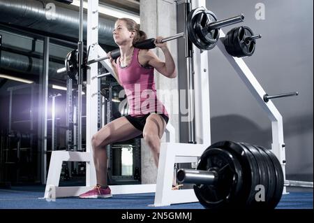 Mid adult woman doing squats barbell on her shoulders in the gym, Bavaria, Germany Stock Photo