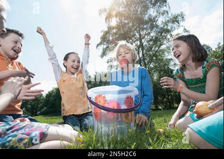 Boy trying to take apple out of a bucket with their mouth, Munich, Bavaria, Germany Stock Photo