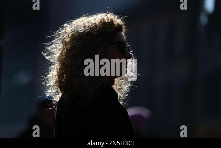 09 February 2023, Hesse, Frankfurt/Main: The curly hair of a woman waiting on a street downtown glows in the backlight. Photo: Arne Dedert/dpa Stock Photo