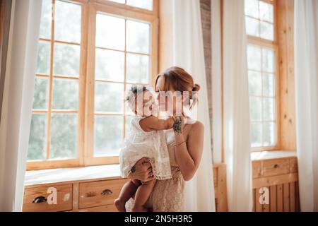 Diverse people portrait of mother with swarthy infant spending time at use light window. Multi ethnic family having fun togetherness enjoying motherho Stock Photo