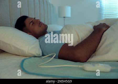 Man sleeping on electric heating pad in bed at night Stock Photo