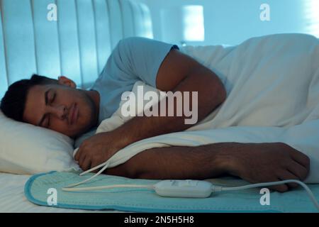 Man sleeping on electric heating pad in bed at night Stock Photo