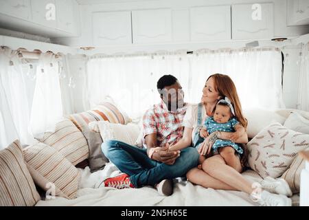 Mixed race smiling family with dark skinned infant daughter spend time together in travel trailer. African american man his fair skin wife and little Stock Photo