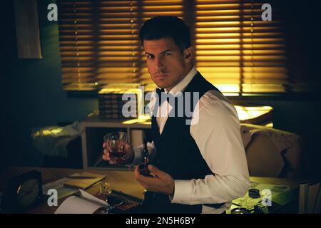 Old fashioned detective with drink and smoking pipe in office Stock Photo