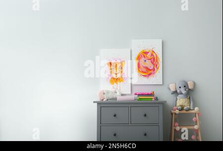 Cute pictures and chest of drawers with toys in baby room interior. Space for text Stock Photo