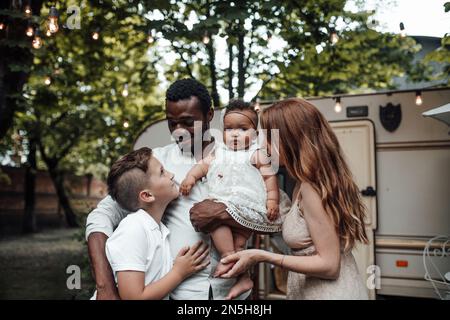 Mixed race family with white son and infant swarthy daughter spend time together in camper park outdoor. African american man with his fair skinned wi Stock Photo