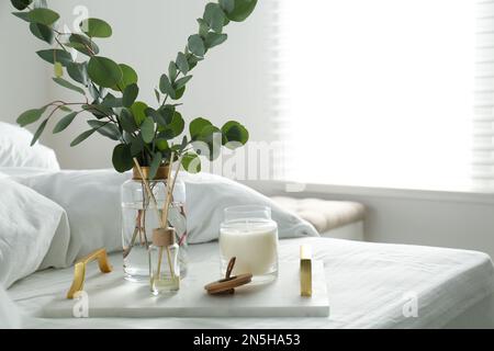 Eucalyptus branches, candle and aromatic reed air freshener on bed indoors, space for text. Interior elements Stock Photo