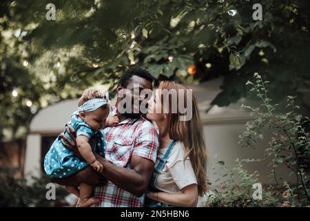 Mixed race family with dark skinned infant daughter spend time together hugs and kisses in camper park. African american man his fair skin wife and li Stock Photo