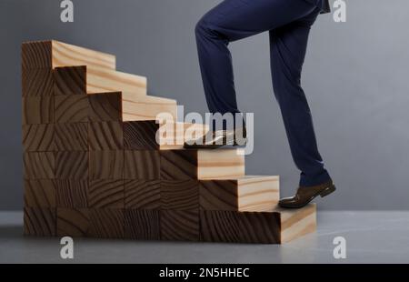 Businessman walking up stairs against grey background, closeup. Career ladder concept Stock Photo