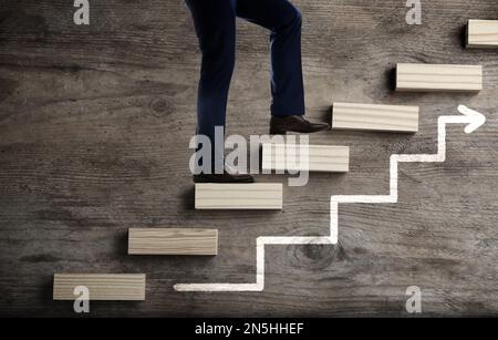 Businessman walking up stairs against wooden background, closeup. Career ladder concept Stock Photo