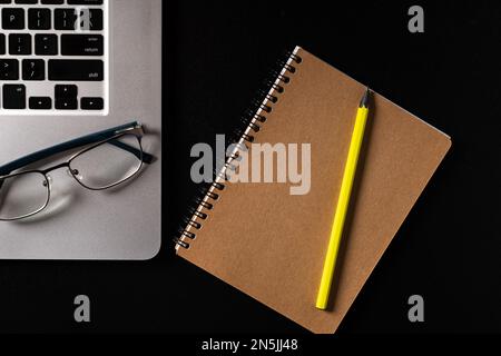 Top view of the desktop. Laptop, glasses, notepad and pencil on black table. Stock Photo