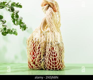 Hand is holding mesh shopping bag with glass bottles with fermented vegetables without plastic bags. Farmers market. Zero waste, plastic free and eco Stock Photo