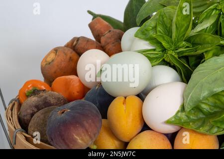 Close-up on organic vegetables in bamboo basket full of fresh vegetables, fruit and eggs from free-range chickens, side view, against white background Stock Photo