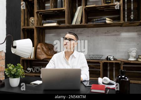 adult caucasian woman with short haircut in glasses works at a laptop in the office Stock Photo
