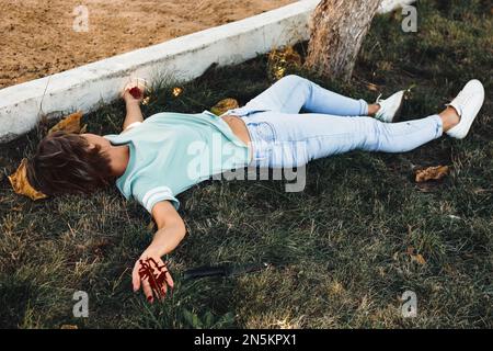 Crime scene with dead woman's body and bloody knife on green grass outdoors. Detective case Stock Photo