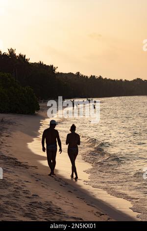 Maldives beach - a couple on a long haul holiday walking at the waters edge on a sandy beach at sunset, Rasdhoo Atoll, The Maldives, Indian Ocean Asia Stock Photo