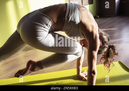 Young woman practicing yoga, doing a variation of Kumbhakasana exercise, straight arm plank with knee raise, exercising in white sportswear in a fitne Stock Photo