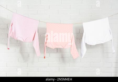 Baby clothes hanging on washing line near white brick wall Stock Photo