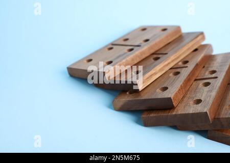 Fallen wooden domino tiles on light blue background Stock Photo