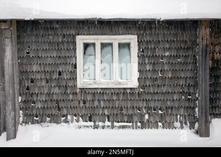 Old window of a old mountain hut and gray wooden wall covered with snow Stock Photo