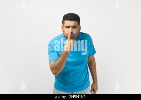 Portrait of unshaven man wearing blue T- shirt looking with incredulous suspicious gaze and touching nose, gesturing you are liar, suspecting falsehood. Indoor studio shot isolated on gray background. Stock Photo