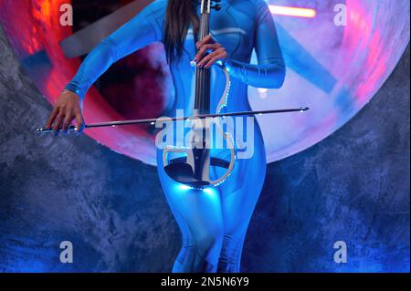 Female musician playing neon glowing electric violin in haze Stock Photo