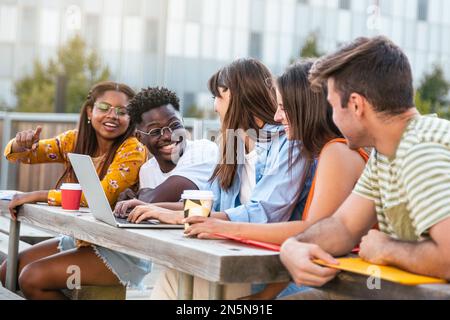 Group of classmates discussing and having fun together, focus on man - students talking laughing and enjoying their time - education concept Stock Photo