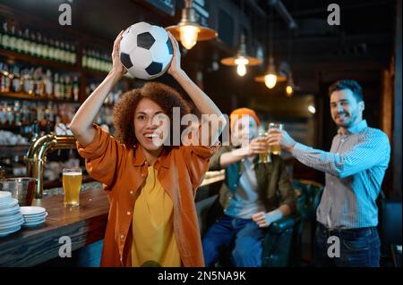 Happy friends rest at sports bar, focus on woman holding soccer ball Stock Photo